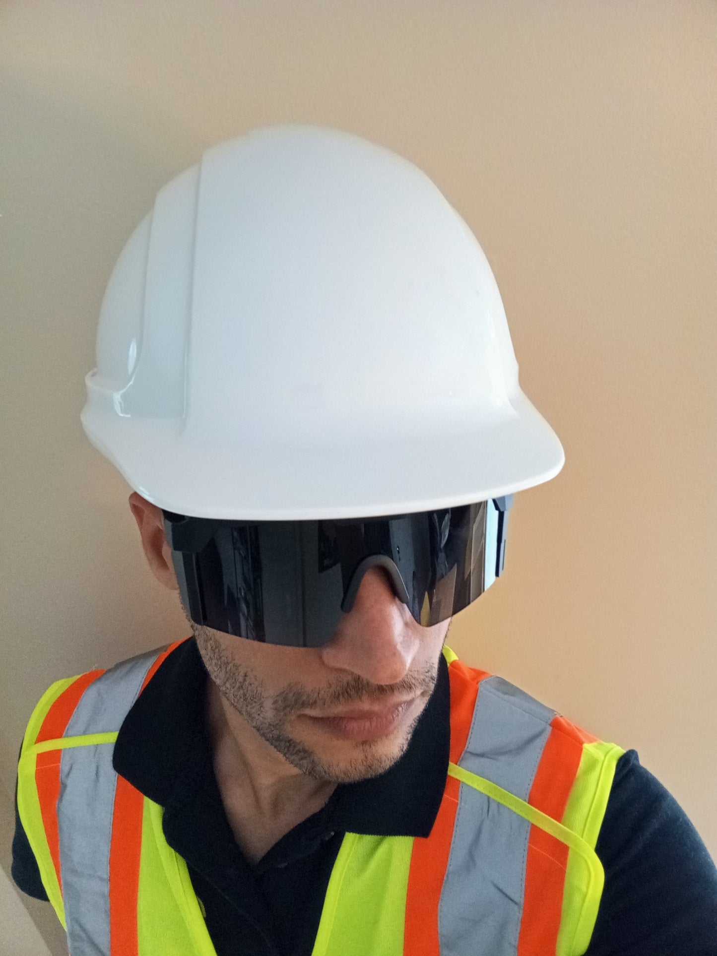 A worker is wearing dark safety sun glasses. He is also wearing a safety helmet and a high visibility vest.