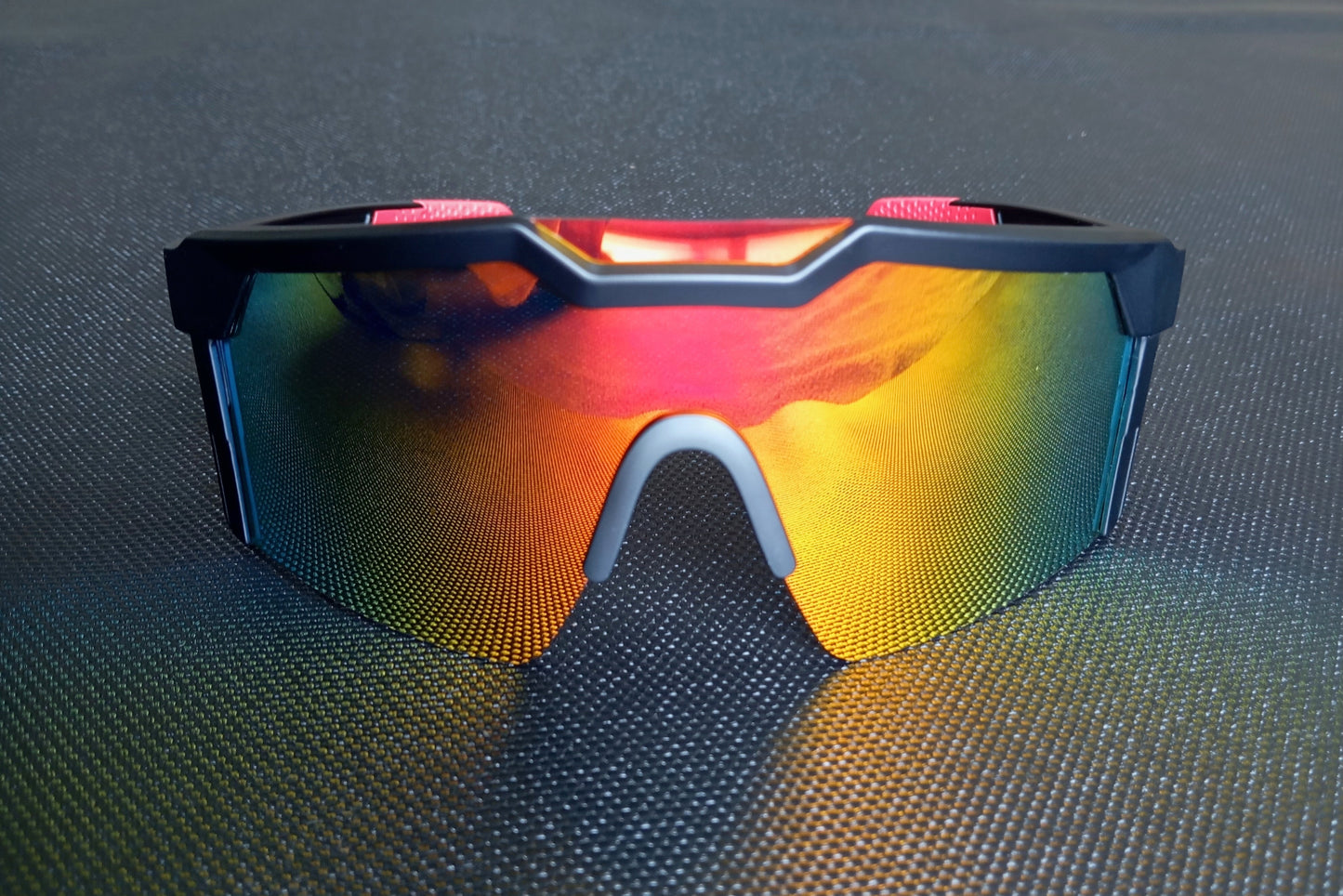 The mirror tinted sunglasses are seen from the front. The light is reflected on the colored polycarbonate lens. Reflections of blue, green, pink and yellow beautifully enhance the sunglasses shape.