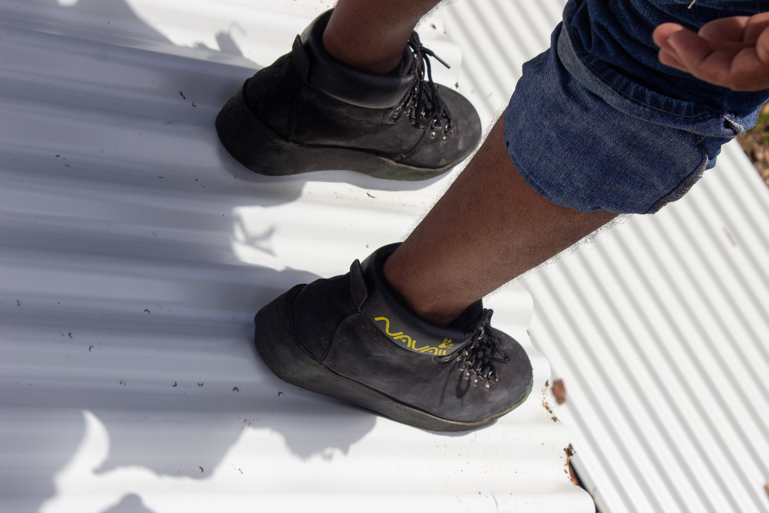 A worker is standing on the edge of a metal roof wearing magnetic non slip shoes