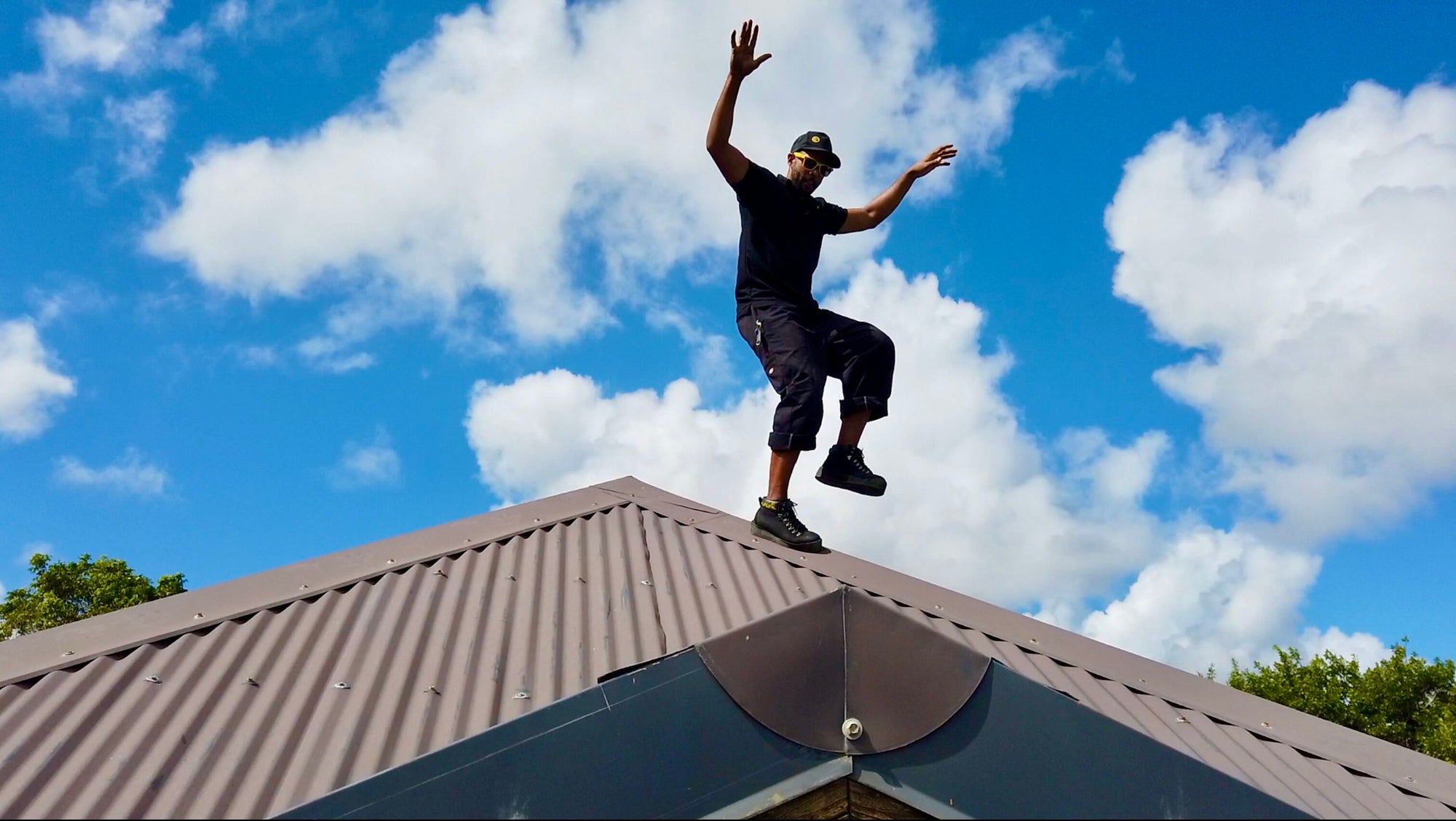 A roofer is wearing magnetic boots on a steel roof. He is standing on a right leg only. He looks confident and safe.