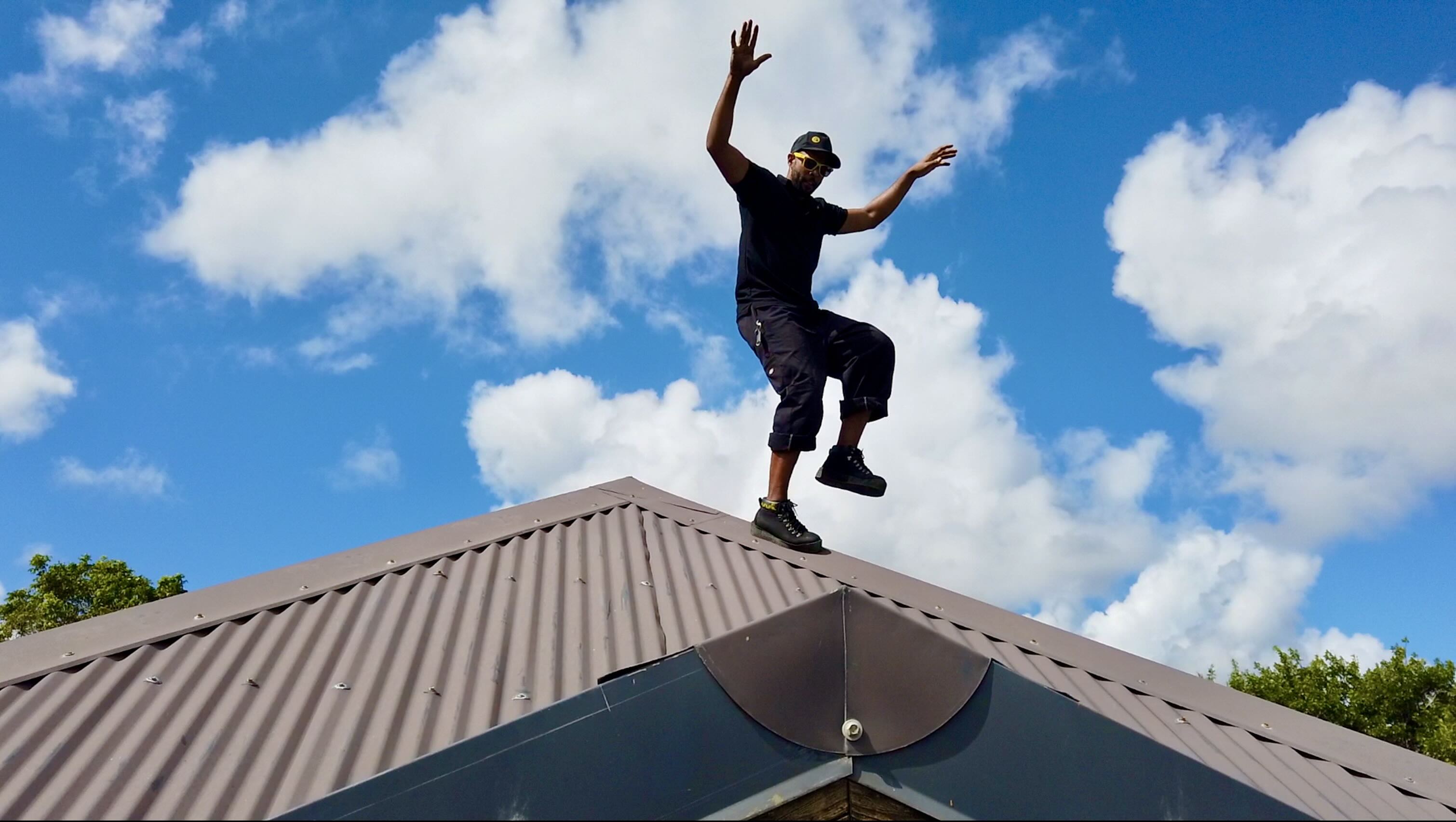 A roofer is wearing magnetic boots on a steel roof. He is standing on a right leg only. He looks confident and safe.